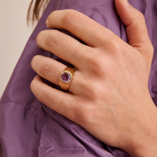 Bague en or jaune 18 carats avec pierre violette sertie portée à la main
